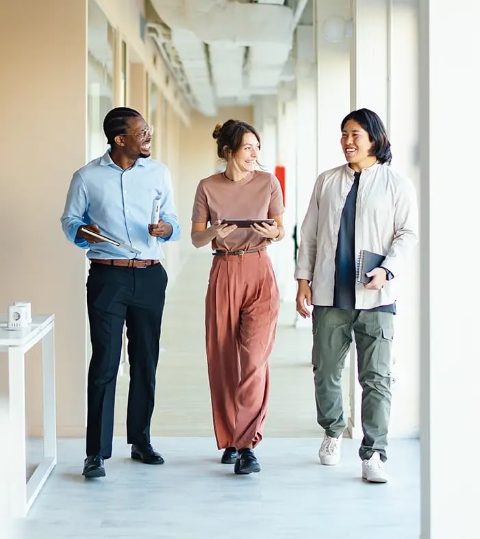 Three colleagues walking and talking in an office hallway